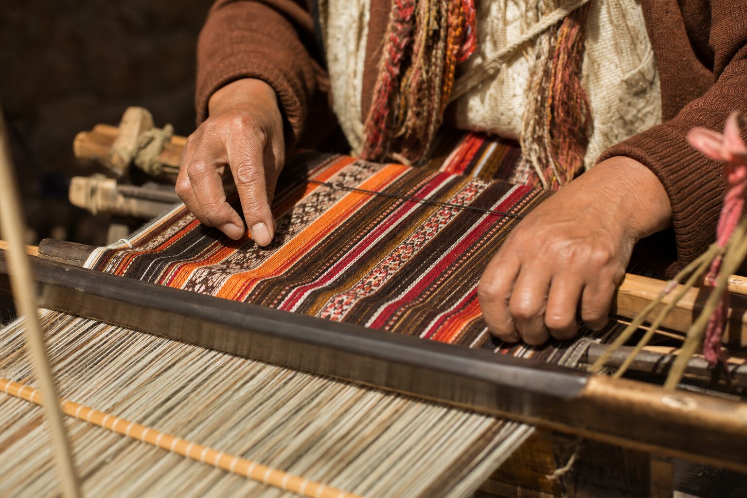 An artisan&rsquo;s hands weaving a colorful textile on a traditional loom